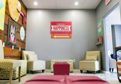 Route 32 Dental kids play room seating area view of wall decoration with animated character on wood planks wall on the left and an office sign: Smile is Happiness on the facing wall